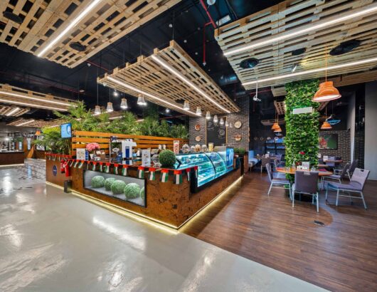 Modern restaurant interior with wooden ceiling, green walls, and a display case filled with pastries.