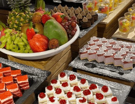 A buffet table displaying a variety of desserts, including cakes, pastries, fruits, and puddings.