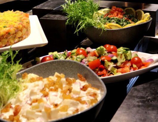 A buffet spread with various salads, including a potato salad, a tomato and cucumber salad, and a green salad.