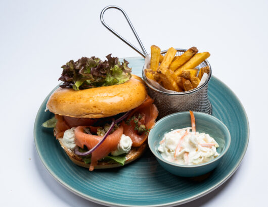 A bagel sandwich with smoked salmon, cream cheese, and lettuce, served with a side of fries and coleslaw.