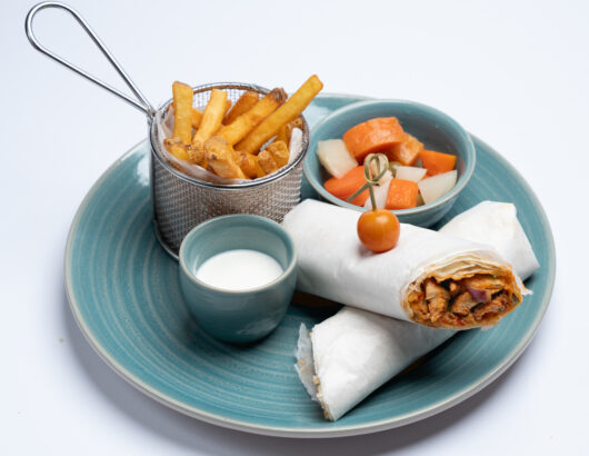 A plate with two chicken shawarma wraps, a side of fries, a small bowl of pickled vegetables, and a dipping sauce.