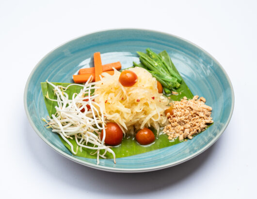 A plate of Som Tum, a Thai green papaya salad with tomatoes, carrots, peanuts, and bean sprouts.
