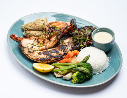 A platter of grilled seafood with prawns, squid, salmon, and fish, served with vegetables and rice.