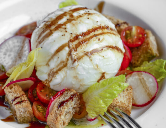 A plate of burrata cheese with cherry tomatoes, radishes, croutons, and a drizzle of balsamic glaze.