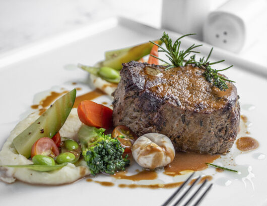 A plate of grilled steak with mashed potatoes, roasted vegetables, and a rich sauce.