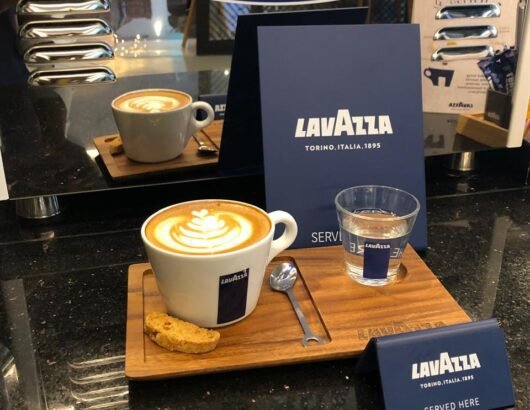 Lavazza coffee with latte art on a wooden tray, served alongside water and biscuits.