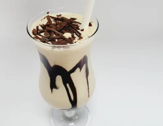 A tall glass of chocolate milkshake topped with whipped cream and chocolate shavings.